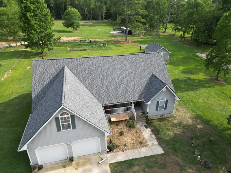 Aerial drone view of a single-story ranch home on acreage after a full shingle roof replacement